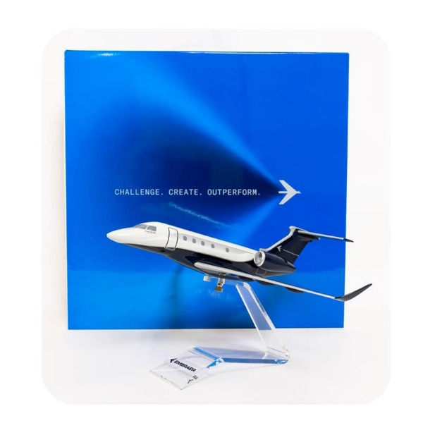 1:72 scale model of the Embraer Praetor 500 jet with acrylic stand in front of blue gift box reading "Challenge. Create. Outperform."