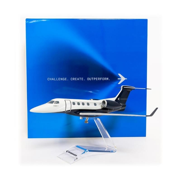 1:50 scale model of the Embraer Phenom 300E executive jet mounted on an acrylic stand with branded box in background.